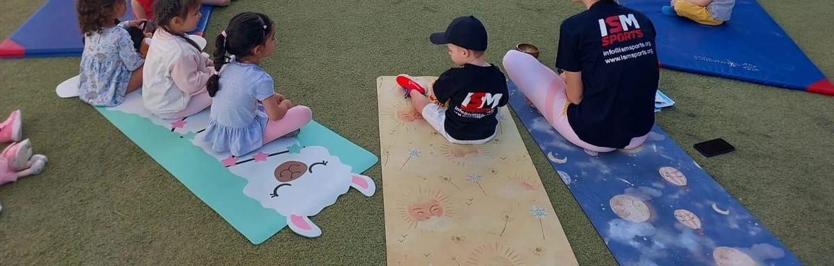 A Little Lions session on mats, the children seen from behind and a coach whose shirt reads ISM Sports.