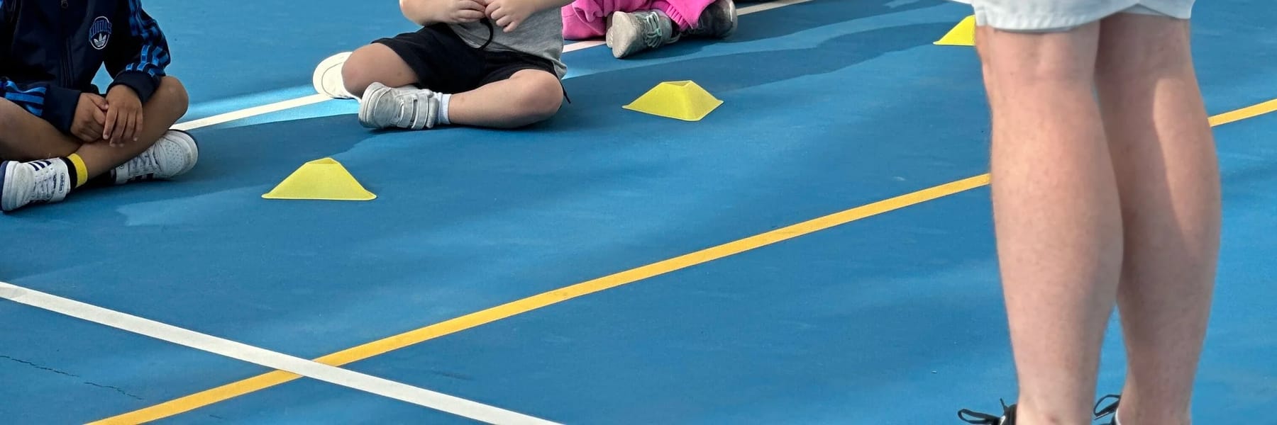Yellow cones on a blue court with players' shoes at the edge of frame.