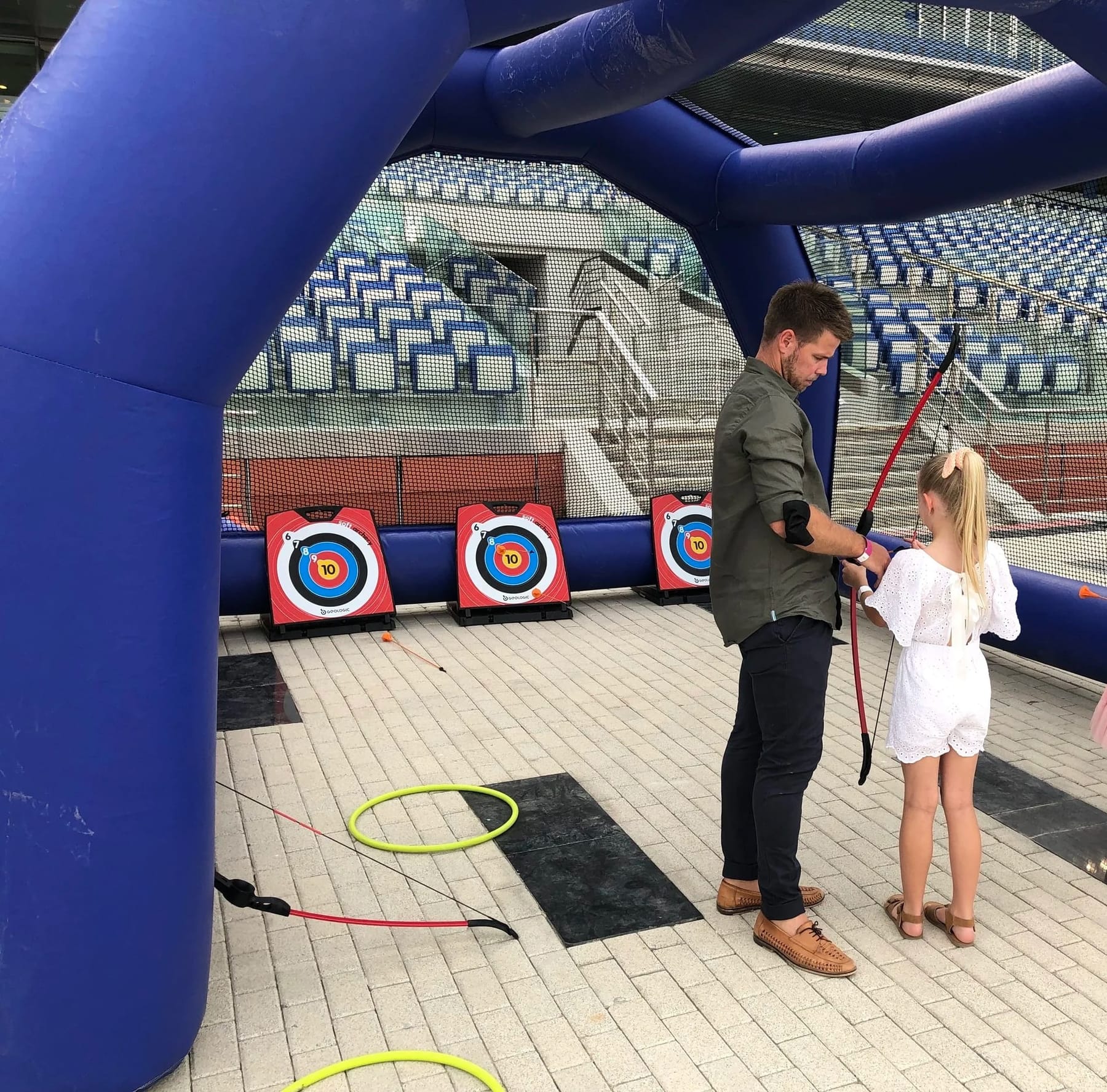 A child seen from behind at an inflatable archery range with a coach.