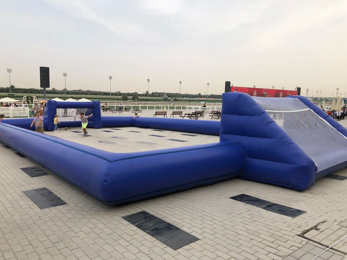 An inflatable pitch on paving with figures far off.