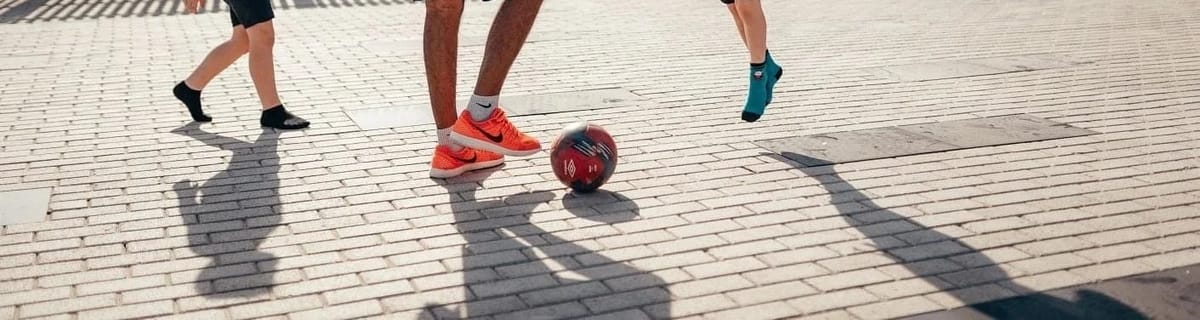 Trainers, a football and long shadows on paving during a session.