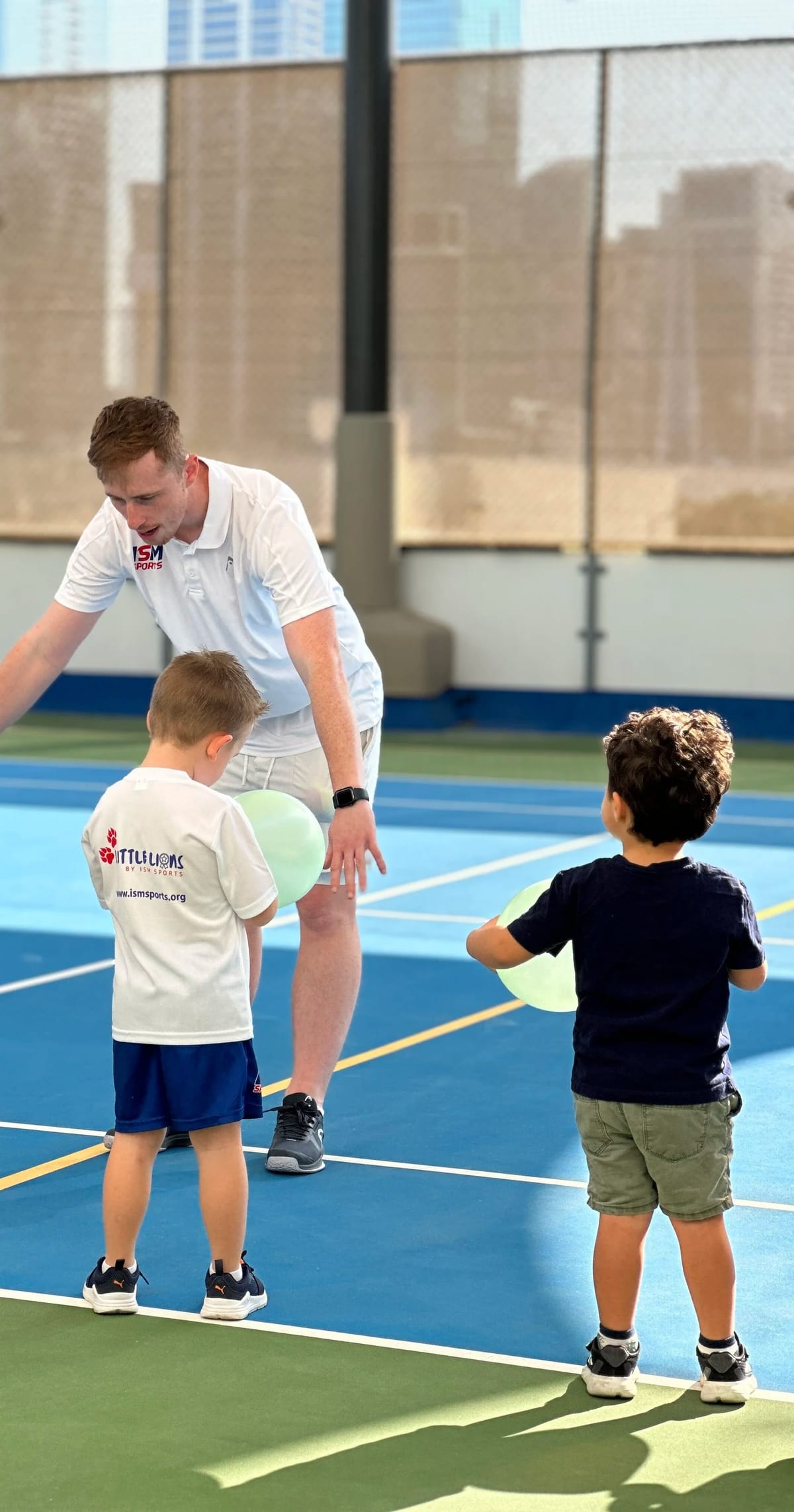 A coach and two small children seen from behind holding balloons.